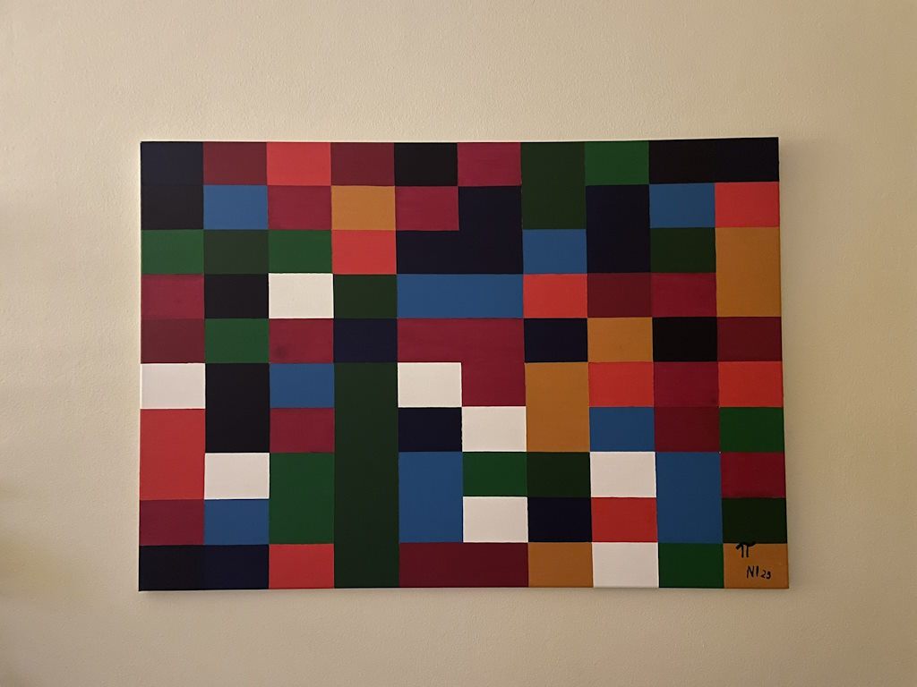 Quadro pendurado numa parede clara: uma grelha de 10 por 10 retângulos pintados em vermelho, bordeaux, verde, azul, azul-escuro, azul-noite, ocre e branco.